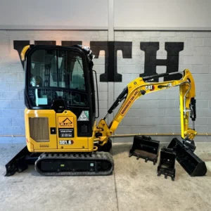 Yellow CAT mini excavator with buckets and attachments in a workshop