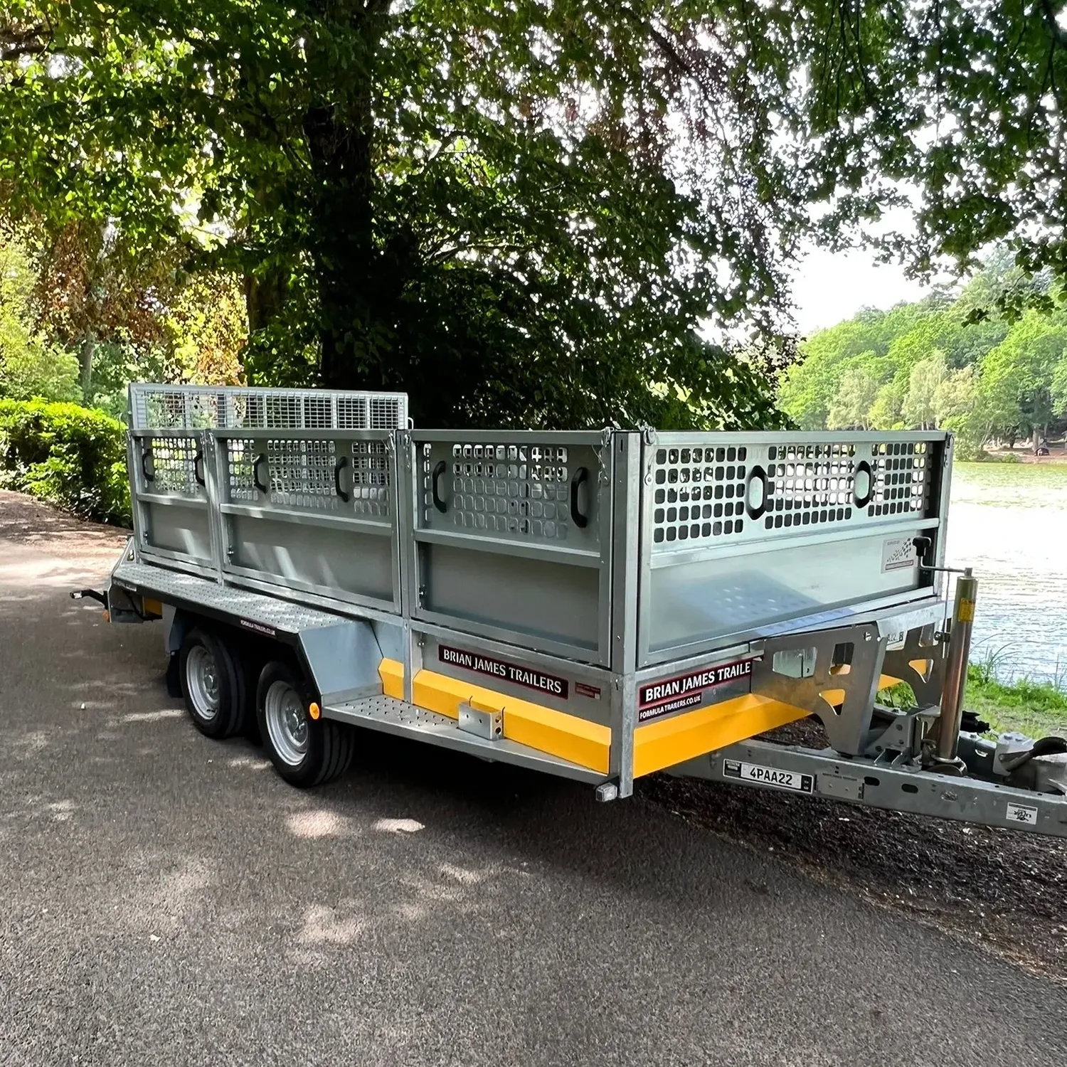 Flatbed trailer parked by a lakeside path under trees