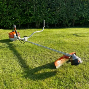 Brush cutter on a lawn with a hedge in the background
