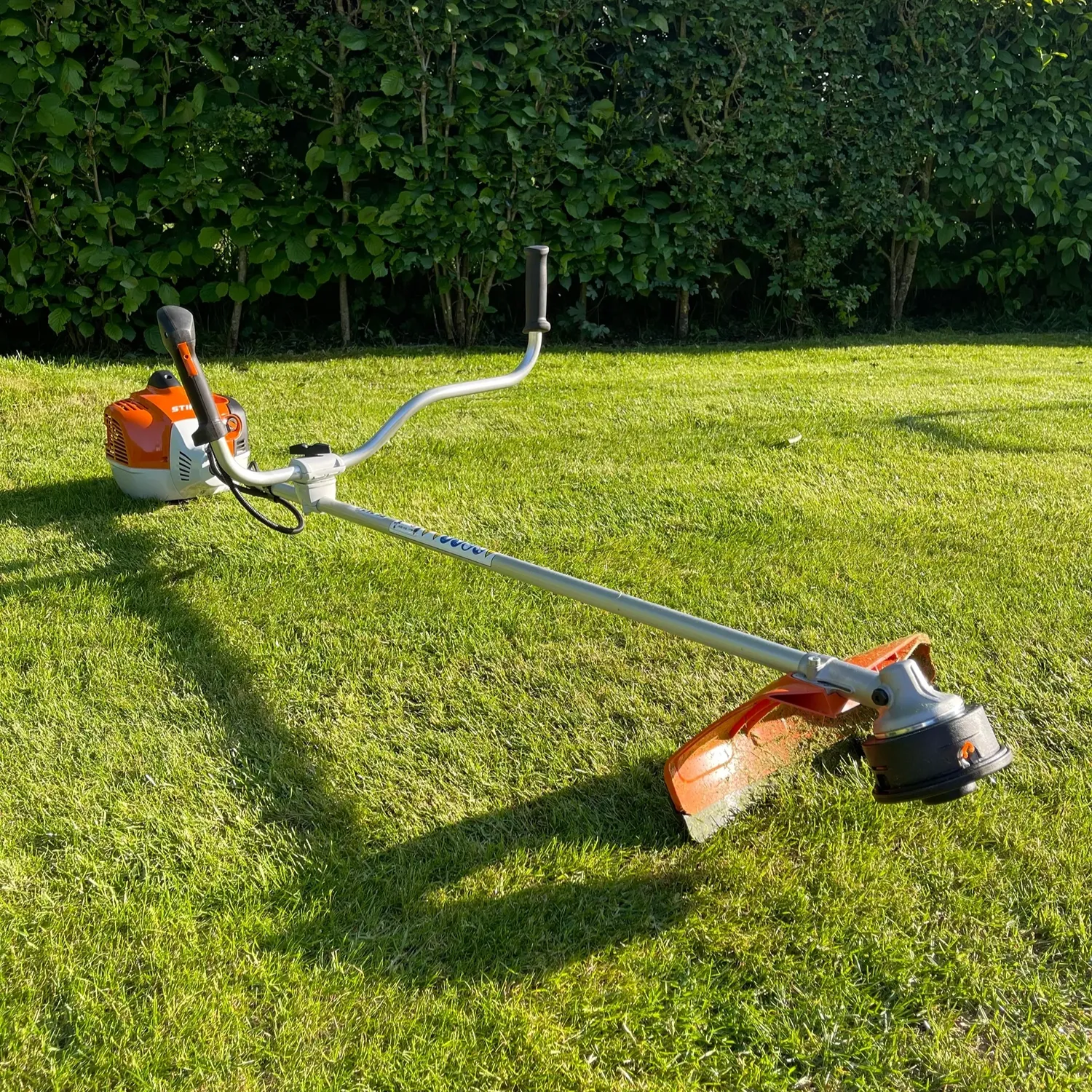 Brush cutter on a lawn with a hedge in the background