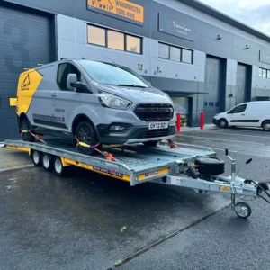 Grey and yellow van strapped to a trailer outside a tool hire warehouse