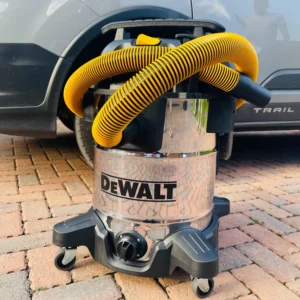 DeWalt wet and dry vacuum cleaner with a stainless steel tank and yellow hose on a brick driveway